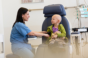 Krebspatientin sitzt auf Behandlungsstuhl und lacht Krankenschwester an.